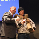 A participant holding a trophy and standing on a stage beside Minister Lafrenière.