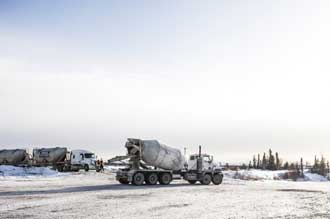 Cette photo montre un camion-malaxeur qui circule sur une route enneigée de l'ancien site minier. Des travailleurs et d'autres camions-malaxeurs sont visibles à l'arrière-plan.